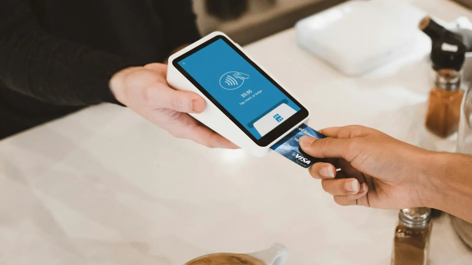 Customer tapping a bank card on a card machine in a coffee shop