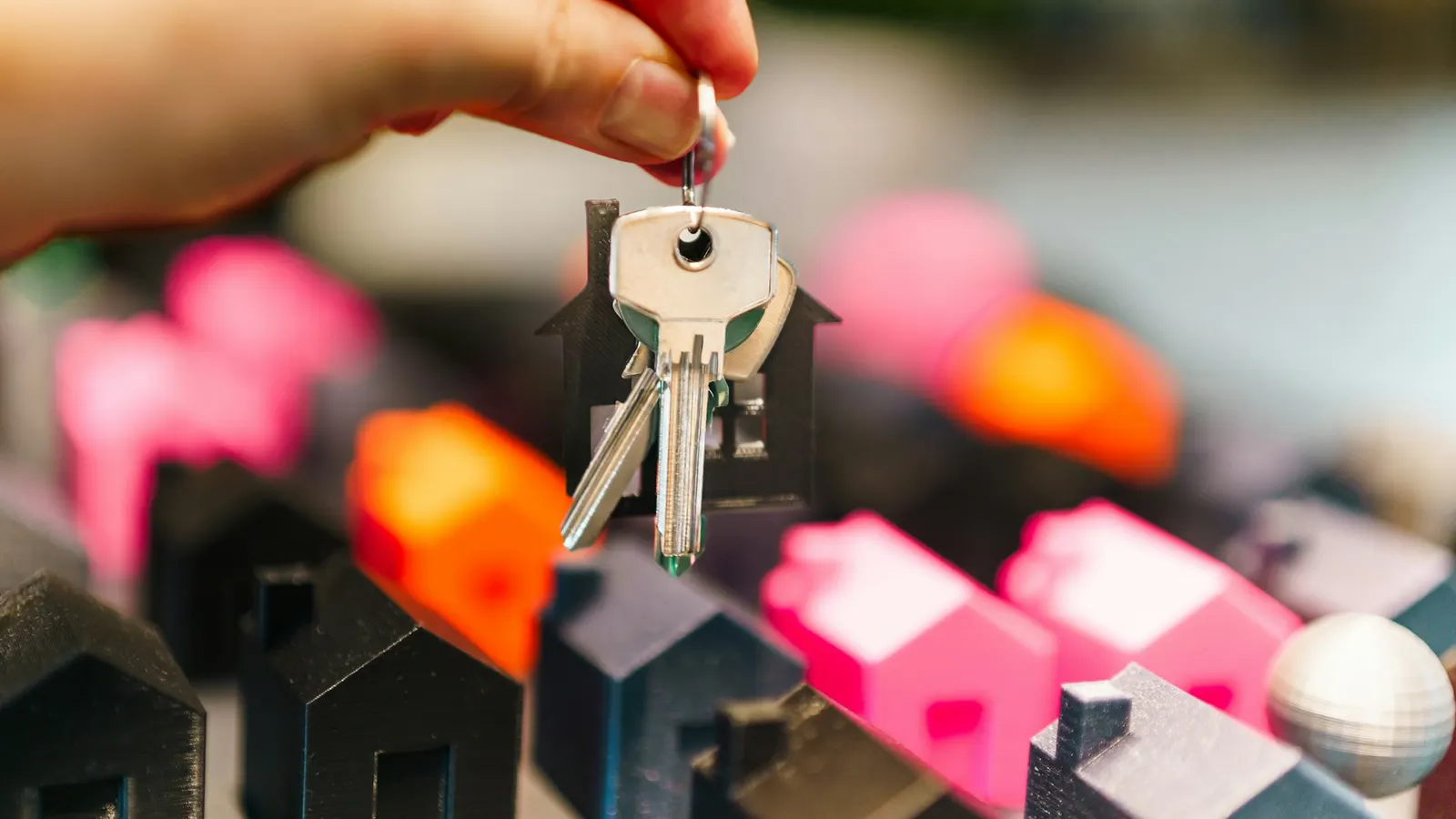 Hand holding house keys above miniature model houses