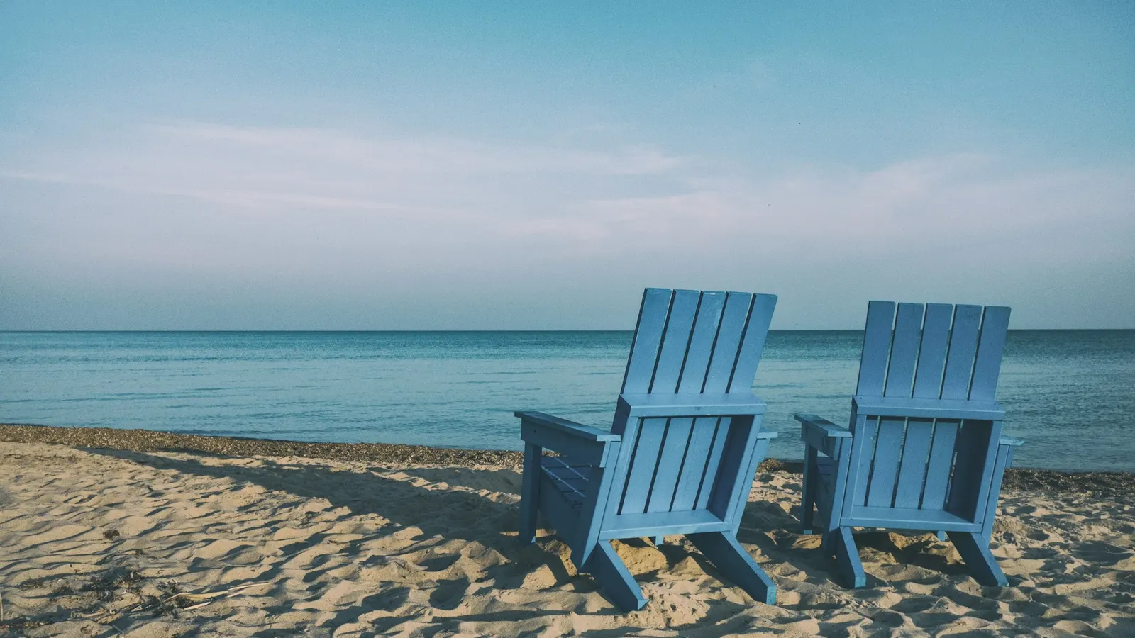 Two blue beach chairs facing the water