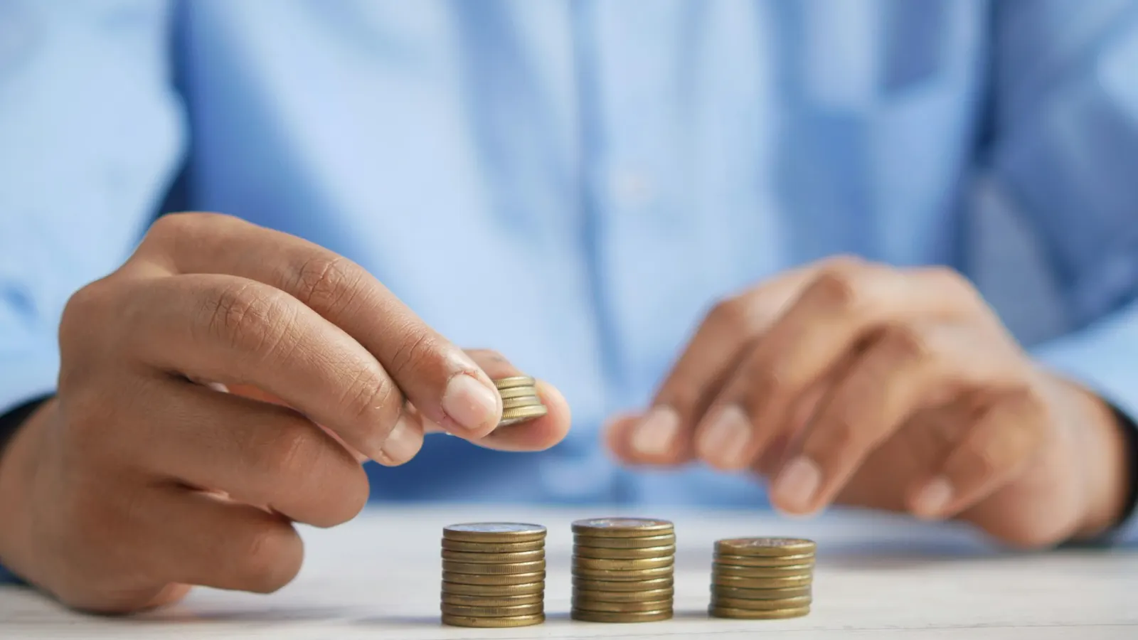 Hand stacking coins into rising piles on a table