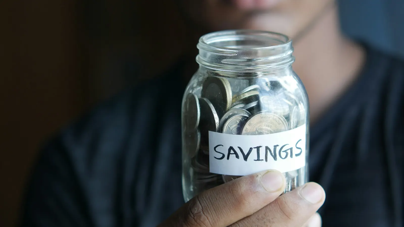 Man holding a glass jar of coins labelled savings